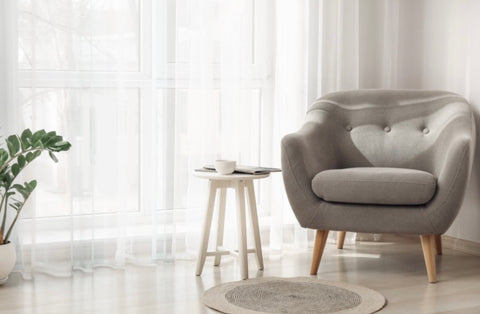 Grey armchair in modern living room with wooden floor sheet curtains and sunlight coming in