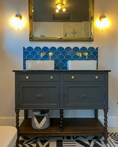 Grey painted bathroom vanity with marble top and two white sinks, gold hardware to match and a walnut colour shelf below 
