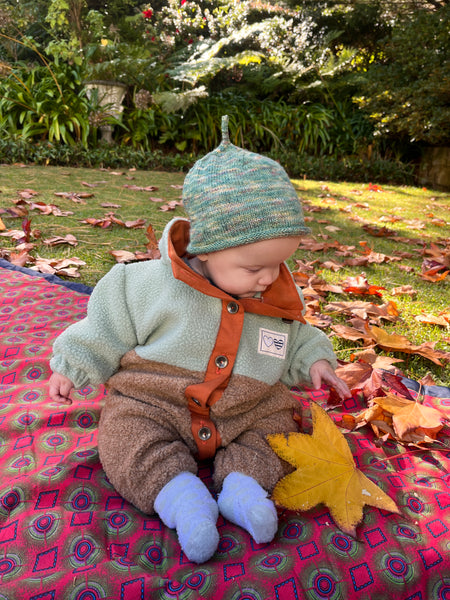 7-month old baby boy wearing fleecy, winter onesie handmade by his mother. He plays with autumn leaves in the garden.