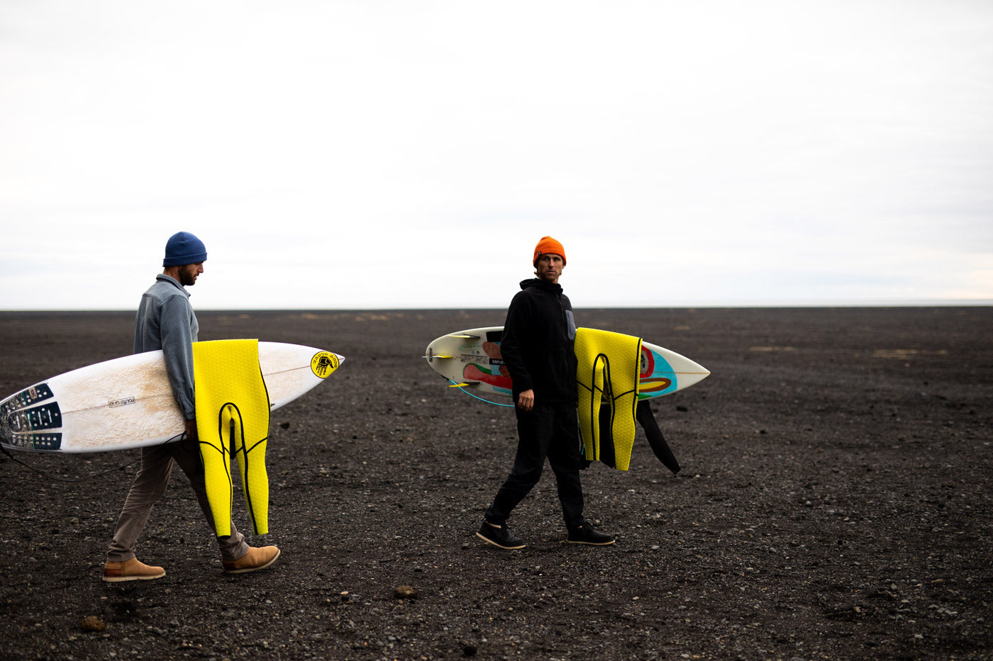 Jesse Mendes walking in iceland with Gold Cell wetsuits on his surfboard
