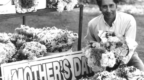 black and white image of Mr Sihota with buckets of carnations next to a mothers day sign