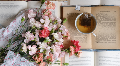 newsletter wrapped carnations arrangement of pastel pinks, peaches and oranges next to an open book and cup of tea
