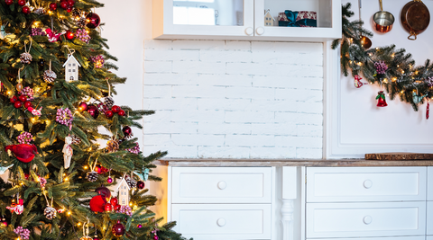 decorated christmas tree to the right of the image with a decorated wreath on the right side and a white wall and some white cabinets in between