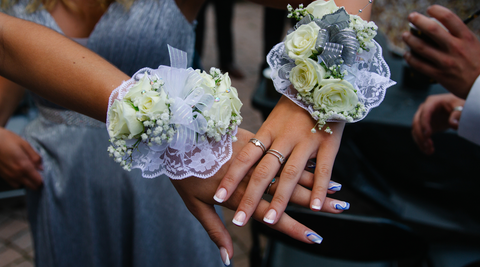 two bridesmaids resting hands on each other showcasing wrist corsages featuring white spray roses as corsage flowers