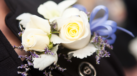 close up of corsage flowers featuring white roses, purple spray and purple ribbons