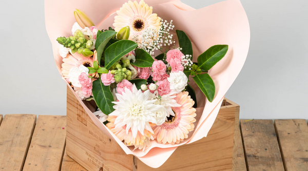 pink and white locally grown flowers wrapped in pink paper with greenery and set on a wooden slatted table
