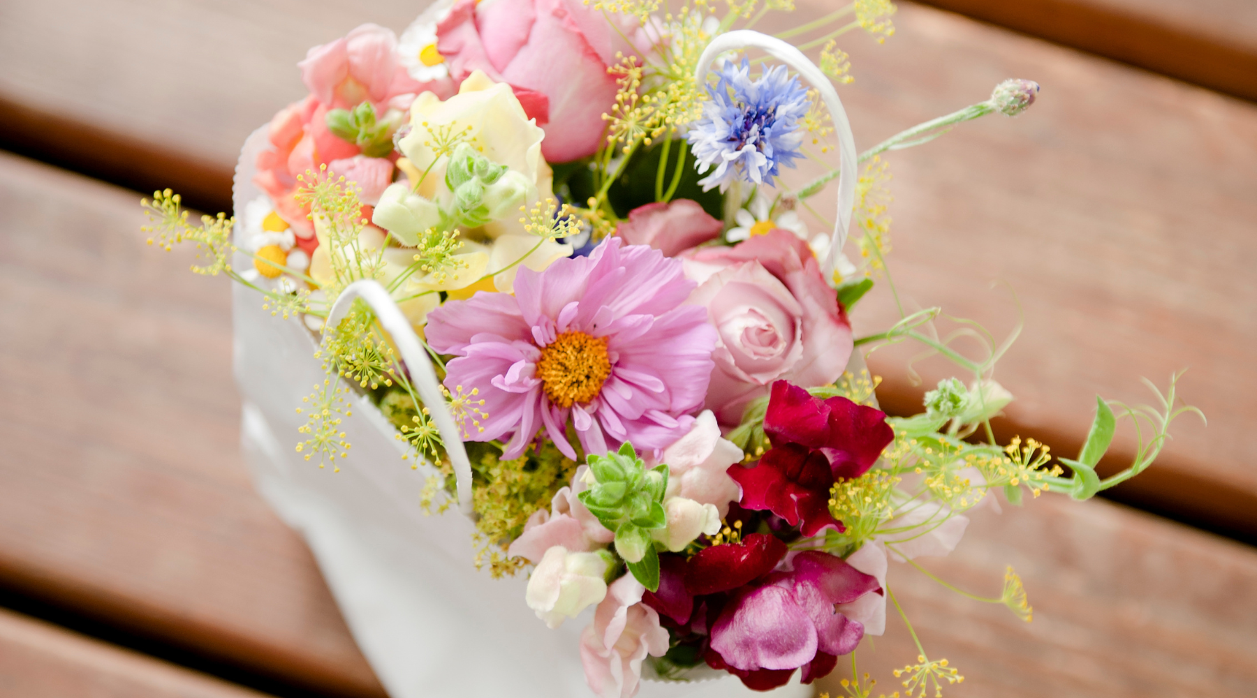 Image of multicoloured blooms in a white basket on a brown wood floor