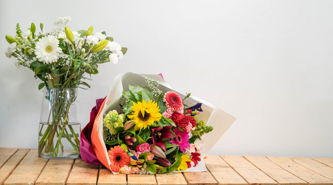 flowers direct from the farm including a white tall arrangement in a glass vase and a multicoloured arrangement wrapped in paper next to it
