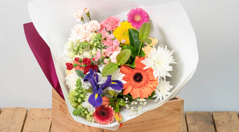 bouquet of multicoloured gerberas on a wooden table wrapped in white paper for flowers with gifts delivery
