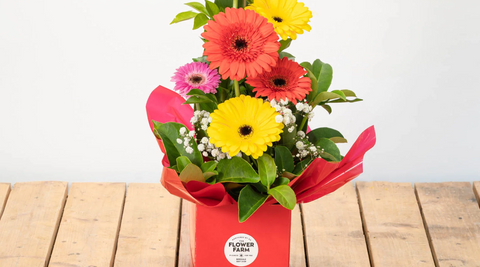 pink, yellow and orange bright gerberas in an arrangment for a new baby with greenery and in a pink box on a wood table