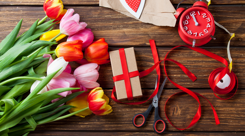 bunch of multicoloured tulips next to a brown paper package with red ribbons next to it for gift wrapping with flowers