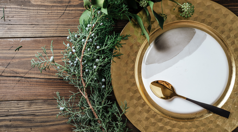close up of a gold and white plate with a gold spoon with pine leaves arranged around it