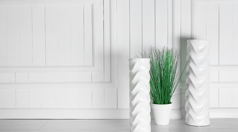 tall white cylinder vases in an entry way next to a round white pot with a plant