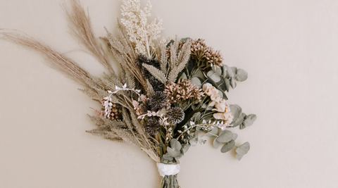air dried flower bouquet with grey greens, peaches and fronds wrapped in a bit of white paper with a peach background for how to preserve flowers
