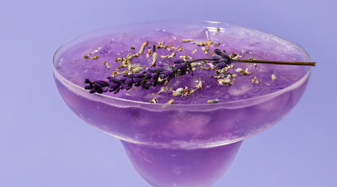 purple flower cocktail in cosmopolitan glass with lavender bloom floating on top against an all purple background