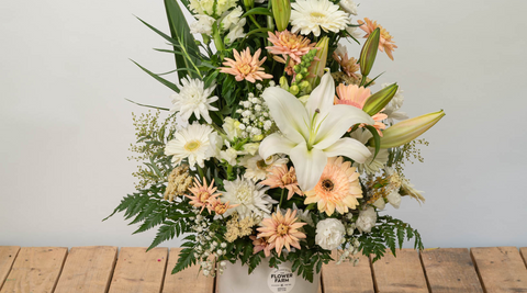 peach and white bouquet with pops of yellow in a white vase on a wooden table featuring lilies in bouquets