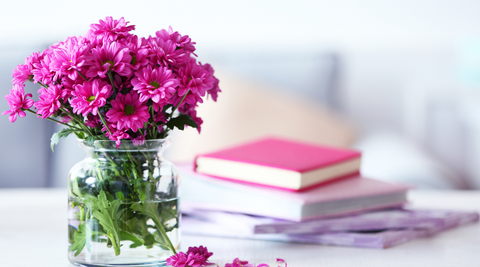 image of pink blooms in wide mouthed, squat glass vase with books stacked next to it