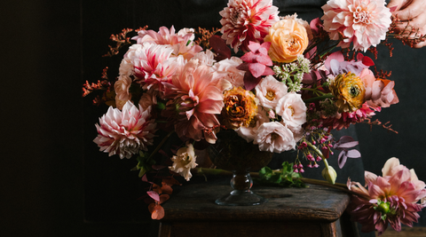 large lush bouquet of pink, peach and blush blooms in a wide vase against a dark black background