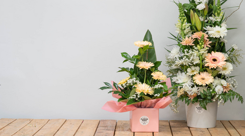 two beautiful and fresh flower arrangements with yellow and pink blooms against a grey background with pink paper demonstrating the benefits of local florists over a flower relay company