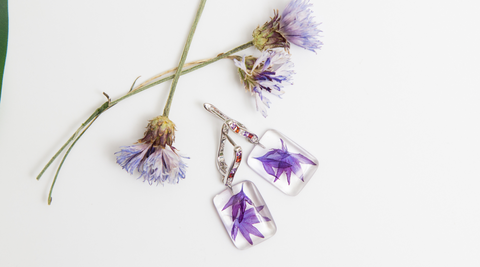 three purple blooms partially dried, and purple flower petals in silica gel made into earrings with jewelled clasps