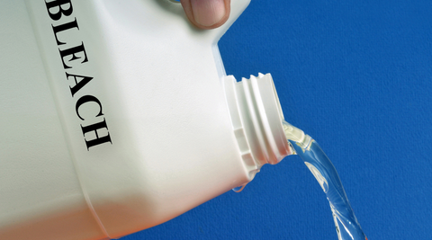 close up of a white bottle pouring out a clear liquid with the words bleach written on the bottle 