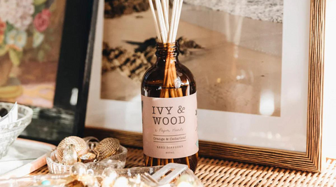 ivy and wood bottle diffuser against a framed photo with jewellery and cut glass bowls around it