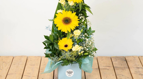 yellow seasonal Flower Farm bouquet with gerberas, mums and baby's breath in a blue box on a wooden table for unique mothers day gifts and flowers