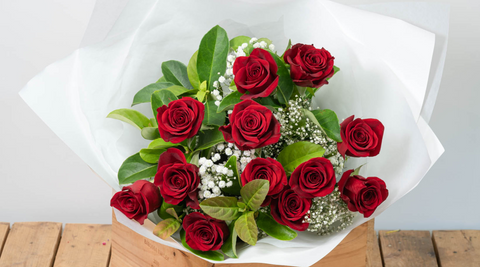 close up image of a dozen red roses wrapped in white tissue and sitting on a wooden slatted table