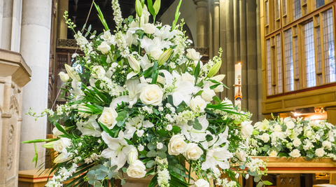 close up of a large all white and green funeral arrangement showcasing what are the best flowers for sympathy set up in a church setting