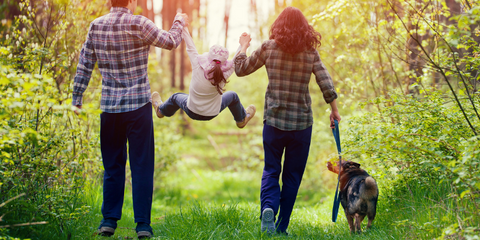 Two parents playing with their child and walking dog outside