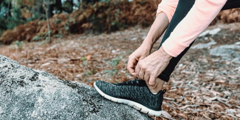 woman resting root on a log and tying shoe