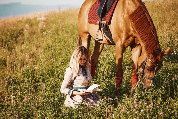 A woman sits and reads near her horse