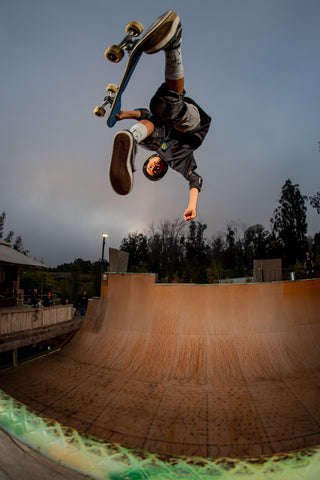 Man upside down while doing a skateboarding trick at a skate park and dropping into the bowl while wearing MERGE4 skate socks.