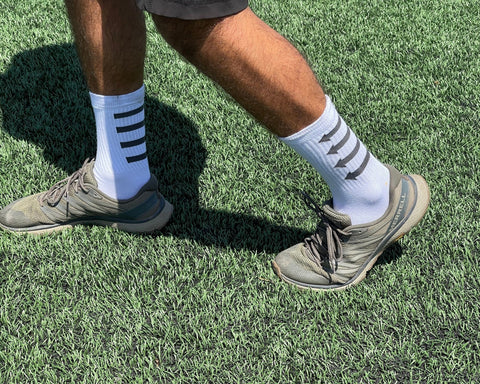 Guy wearing running shoes on a turf field while wearing MERGE4 white training socks.