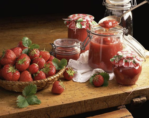 sweet and savory jams, in glass jars next to a bowl of strawberries 