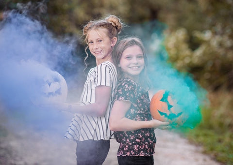Two girls holding pumpkins with smoke. Blue smoke and turquoise smoke produced by colorful smoke grenades