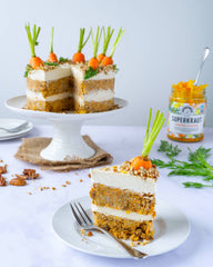 Carrot cake, with a slice on a smaller plate in the foreground, accompanied by Turmeric & Ginger Superkraut in the background