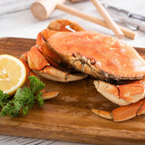 A freshly prepared Dungeness crab displayed on a wooden cutting board, accompanied by a vibrant slice of lemon and sprigs of parsley. In the background, wooden crab mallets and seafood crackers await the delightful feast.