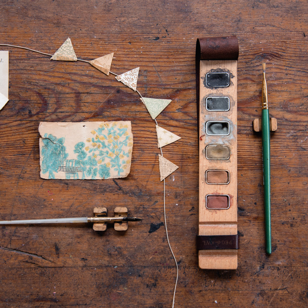 wooden paint palette on wooden desk with pen rests and vintage dip pen