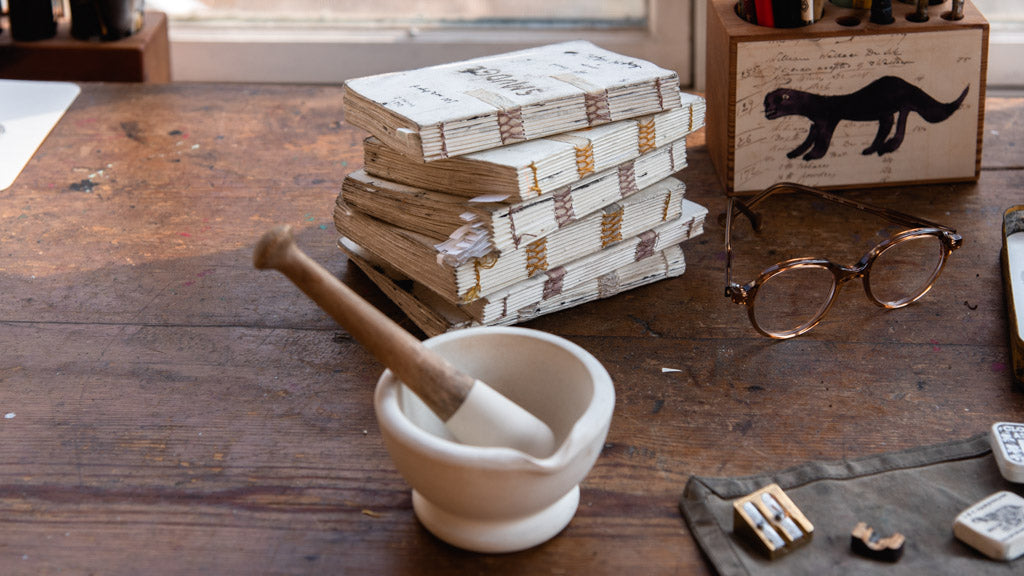 stack of handmade paper sketchbooks on desk with mortar and pestle  