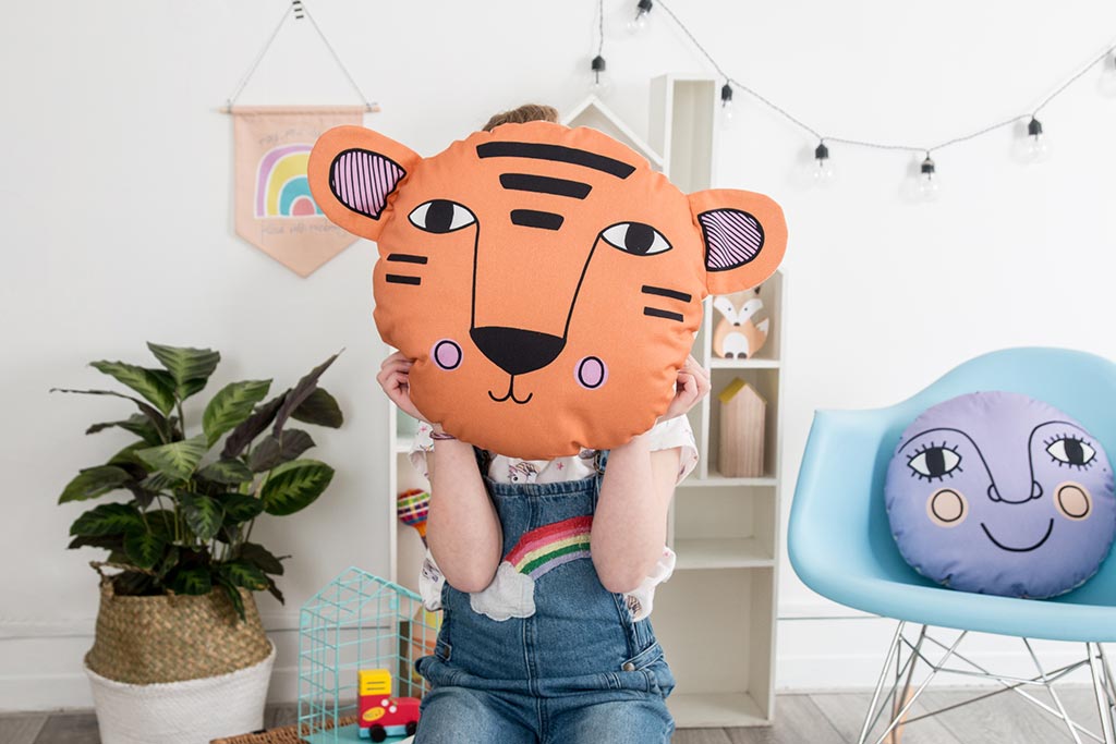 A cute tiger face cushion being held up in front of the face of a kid