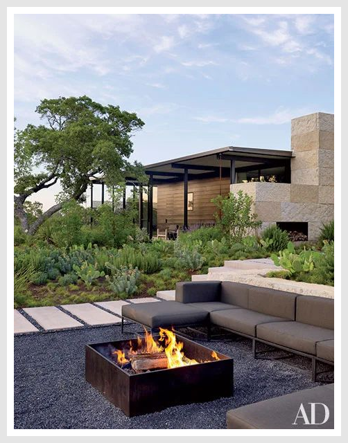 Outdoor fireplace with seating area and greenery in the background.