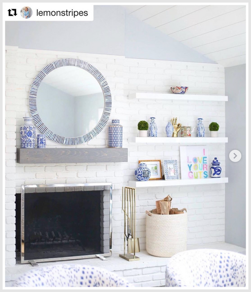 A room with a white brick wall pattern, capiz mirror above the fireplace and various decorative items on shelves.