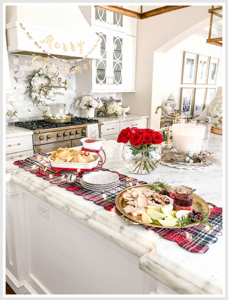 A table set for Christmas with white plates, greenery, candles, and gold accents. Red berries and pinecones add a festive touch.