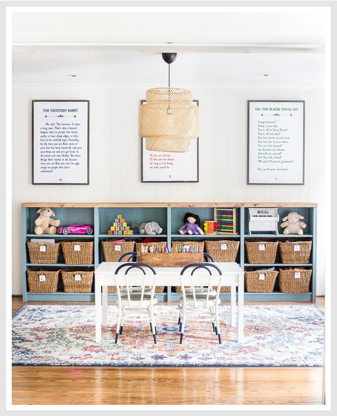 White dining table with a woven pendant light above it, cubbies in the background.