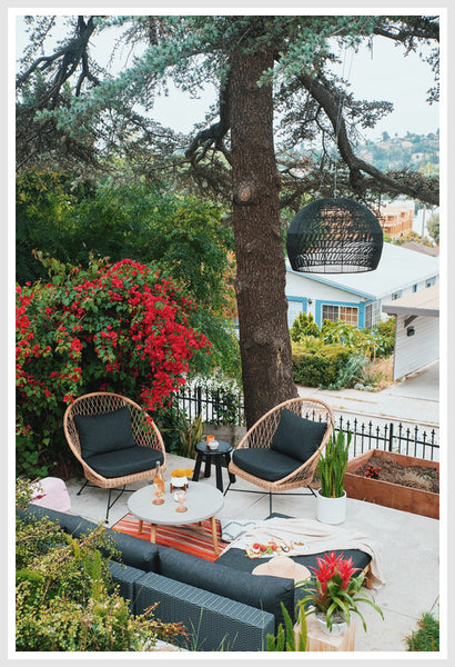 2 Rattan chairs with dark cushions outdoors, pendant light above them