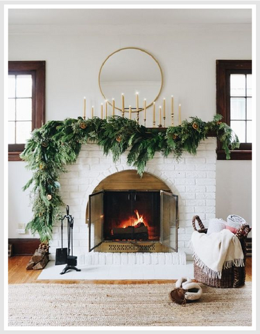 An indoor fireplace with greenery and candles on the mantle.