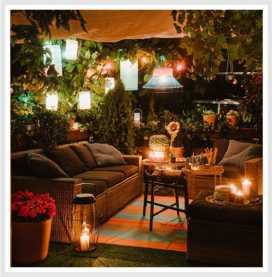 Cozily-lit outdoor area with sofa and various lighting fixtures and lanterns.