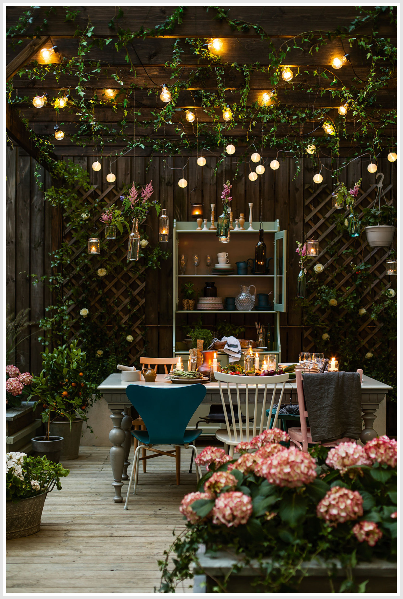 Outdoor lighting fixtures and a table with chairs in a garden setting with trees and bushes in the background.