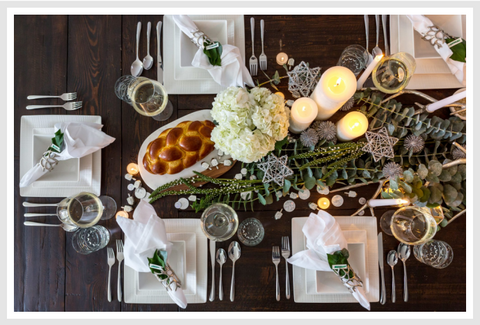 A table setting with square plates, tableware and candles.